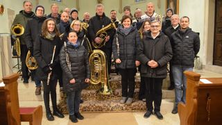 Eine Gruppe von Musikern, darunter Trompeten, Posaunen und Klarinetten, posiert für ein Foto in einer Kirche.