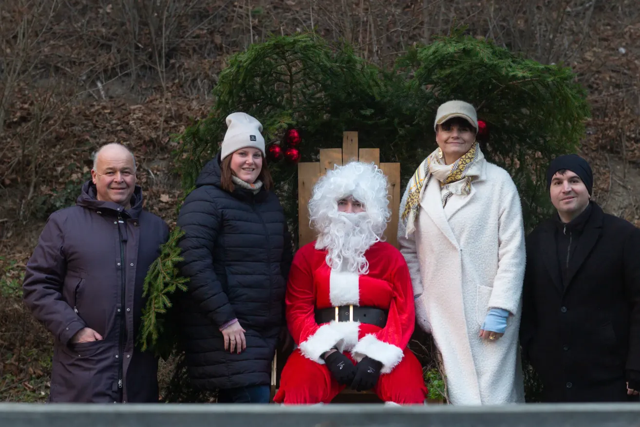 A group of people, including a person in a Santa Claus costume, are standing in front of a Christmas tree. They are smiling and posing for a photo.