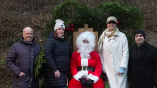 Eine Gruppe von Menschen, darunter eine Person in einem Weihnachtsmannkostüm, steht vor einem Weihnachtsbaum. Sie lächeln und posieren für ein Foto.