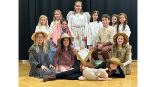 Eine Gruppe von Kindern in Kostümen posiert für ein Foto mit einer Babypuppe, einem Stoffschaf und einem hölzernen Kreuz in einer inszenierten Krippenszene.