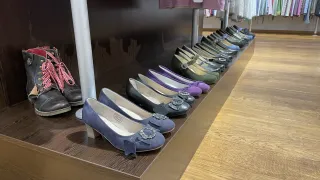 Ein Holzregal zeigt eine Reihe von Damenschuhen in verschiedenen Farben. Die Schuhe haben dekorative Schnallen und Bänder.