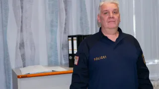 Ein Mann in einer blauen Polizeiuniform steht in einem Büro, mit einem weißen Vorhang und Büchern im Hintergrund.
