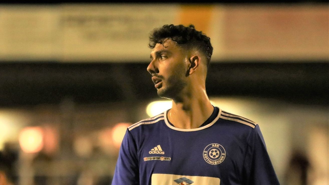 Ein männlicher Fußballspieler in einem blauen Trikot mit Adidas- und Kottingbrunn-Logos schaut während eines Spiels bei Nacht nach vorne.