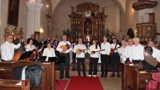 Eine Gruppe von Musikern in weißen Kleidungsstücken, die Gitarren spielen, steht vor einem Altar in einer Kirche.