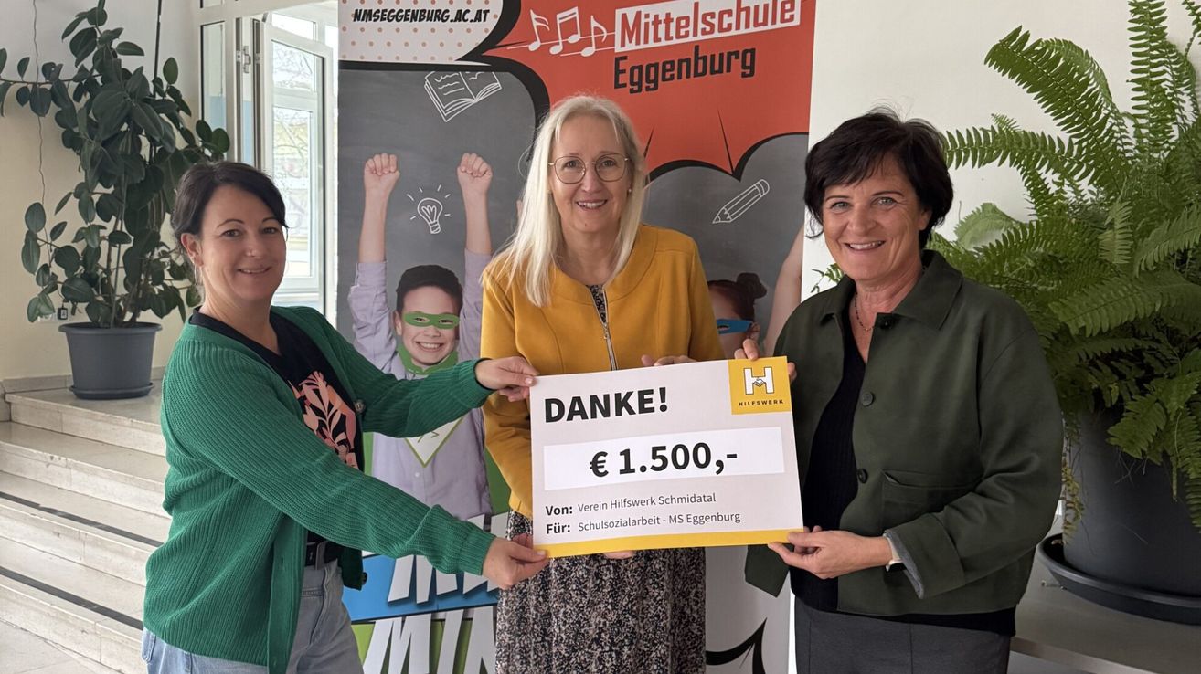 Drei Frauen stehen vor einem Banner. Eine hält einen Scheck über 1.500 € von Verein Hilfwerk Schmidatal für Schulsozialarbeit an MS Eggenburg.