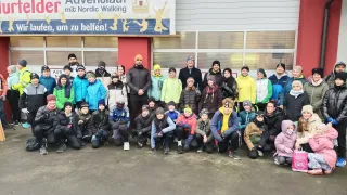 Eine Gruppe von Menschen in Winterkleidung steht vor einem Gebäude mit einem Banner, auf dem 'Willkommen zum Adventlauf mit Nordic Walking' steht. Sie posieren für ein Foto.