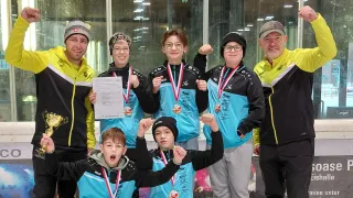 A group of people wearing medals and holding a certificate, smiling for a photo in an indoor setting.