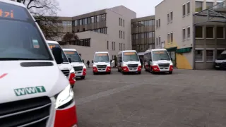 Fünf weiße und rote Busse sind vor einem Gebäude geparkt. Die Busse haben digitale Anzeigen auf der Vorderseite.