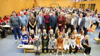 Eine große Gruppe von Erwachsenen und Kindern in Festkostümen posiert für ein Foto in einer Turnhalle, wobei einige Masken tragen und einige hinter einer Holzbank stehen.