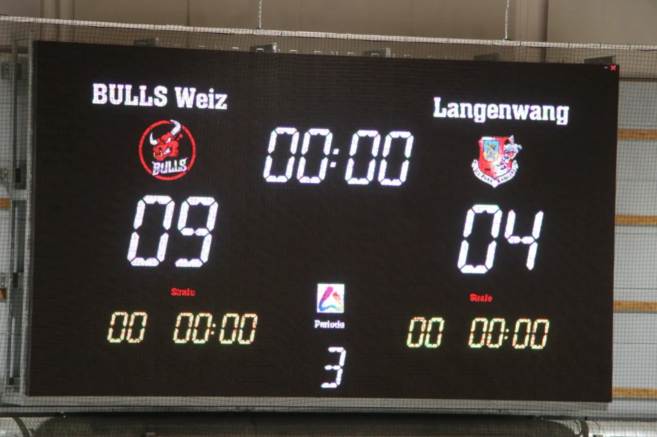 Ein Anzeigetafel zeigt ein Sportspiel zwischen Bulls Weiz und Langenwald mit den Ergebnissen 09 und 04. Das Spiel befindet sich in der dritten Periode, und die Uhr zeigt 00:00 an.
