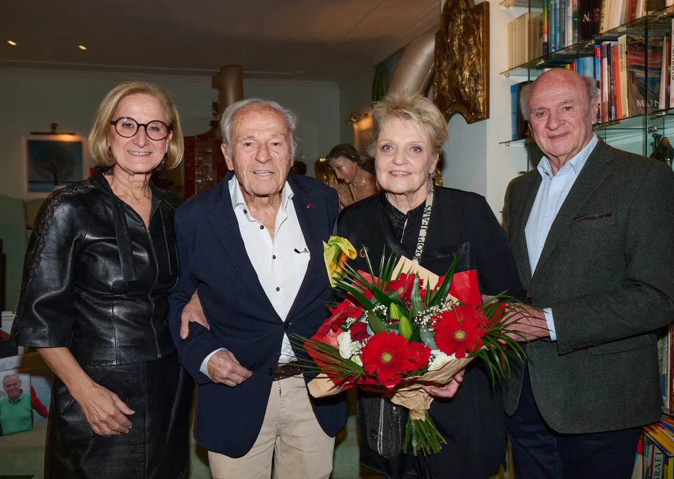 Vier Menschen stehen zusammen in einem Raum. Ein Mann und eine Frau halten einen Blumenstrauß, während eine Frau mit Brille links steht.
