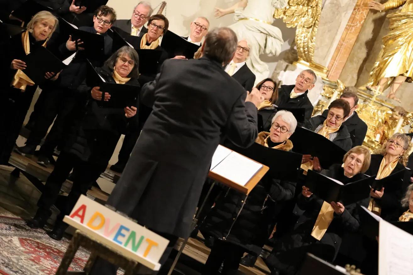Ein Chor singt bei einem Adventsgottesdienst. Die Chormitglieder halten Musikbücher. Der Dirigent steht vor dem Chor. Der Chor trägt schwarze und gelbe Schals.