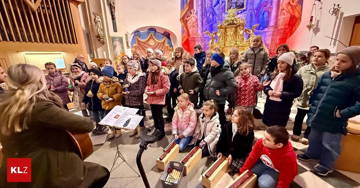 Eine Gruppe von Kindern und Erwachsenen versammelt sich in einer Kirche, einige sitzen auf dem Boden, andere stehen, halten Musikinstrumente und singen.