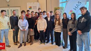 Eine Gruppe von Personen, einschließlich Erwachsener und junger Menschen, posiert für ein Foto vor Bannern. Sie stehen gemeinsam auf einem gefliesten Boden.