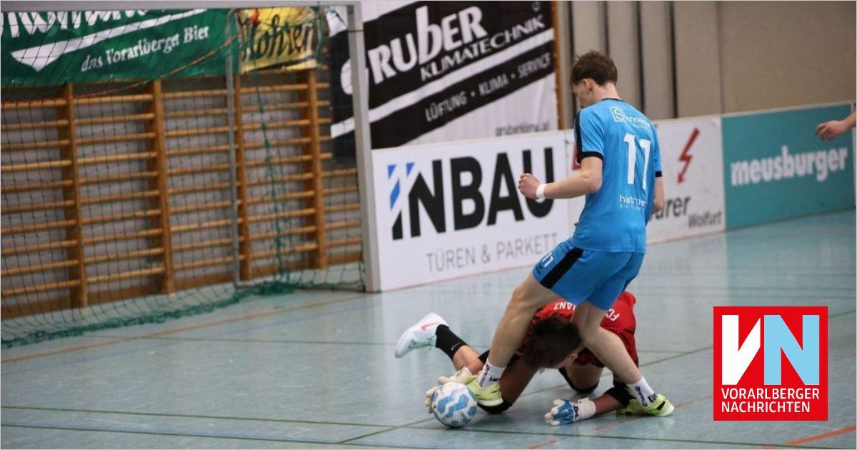 Zwei Männer spielen Futsal in einer Halle. Der Spieler in Blau trägt das Trikot mit der Nummer 11 und ist dabei, den Ball zu schießen. Der Spieler in Rot liegt auf dem Boden.
