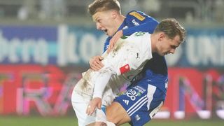 Two soccer players in blue and white jerseys are in a close match on the field, grappling intensely.