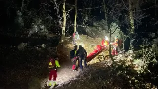 A nighttime rescue operation in a forest with several people wearing safety suits, one pushing a stretcher with a patient.