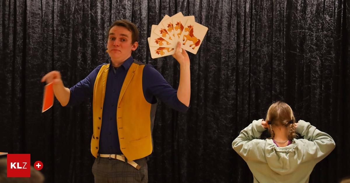 A man in a blue shirt and yellow vest is holding cards with horse images in front of a black curtain, while a young girl watches.