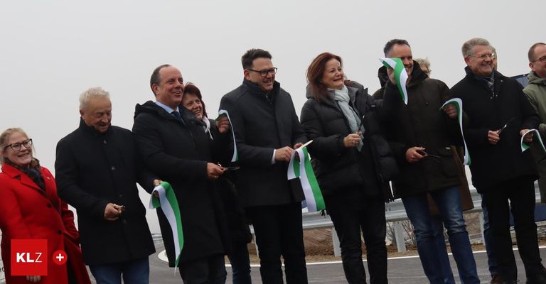 Eine Gruppe von Menschen steht auf einer Straße, hält grüne und weiße Bänder und lächelt für die Kamera, gekleidet in Winterkleidung.