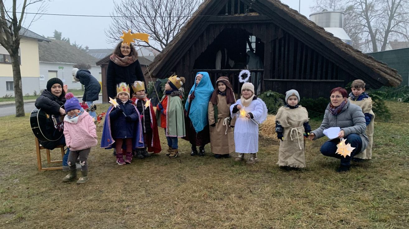 Kinder in Kostümen der drei Weisen stehen vor einer Krippe. Eine Frau hält einen Stern.