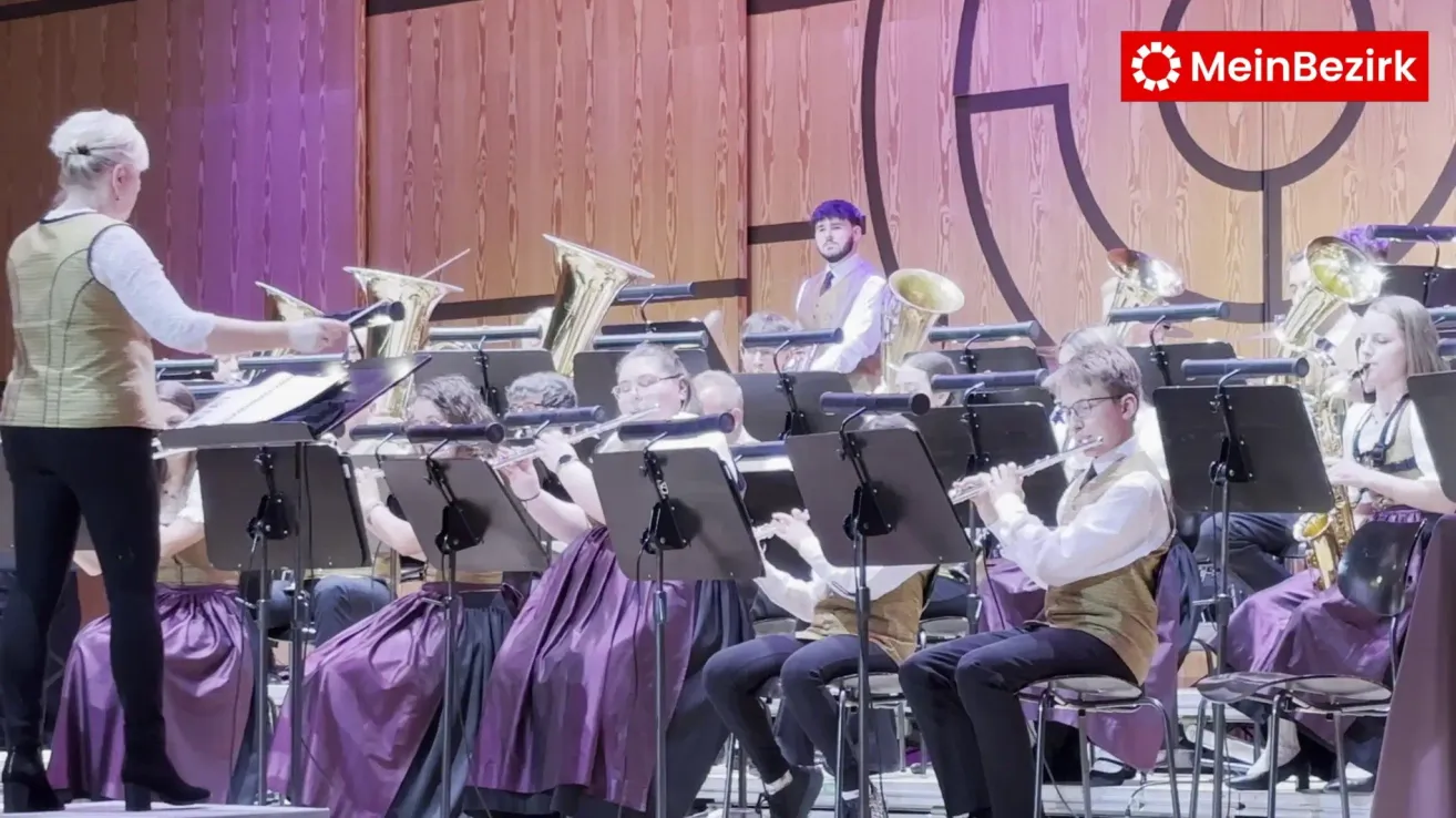 Eine Band spielt auf der Bühne, mehrere Musiker spielen Instrumente wie Flöten, Trompeten und Posaunen. Das Publikum sitzt davor.