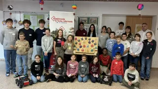 Eine Gruppe von Schülern steht um ein Display-Board mit verschiedenen Pins und Abzeichen herum. Sie stehen und sitzen auf dem Boden und tragen Freizeitkleidung. Einige Schüler halten kleine Roboter.