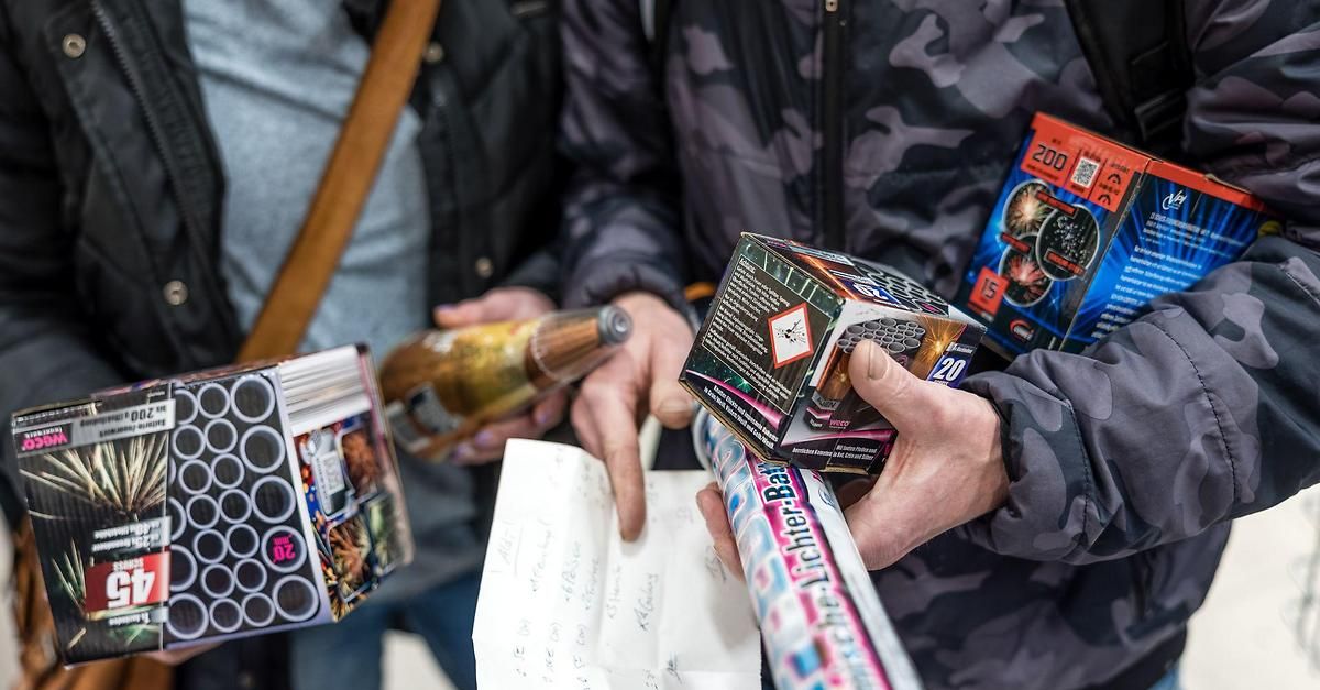 Zwei Personen betrachten Feuerwerk in ihren Händen, einer trägt eine Tarnjacke und der andere eine schwarze Jacke.