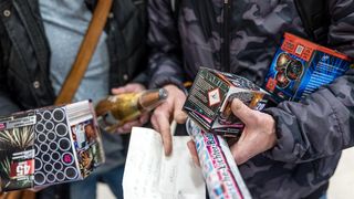Zwei Personen betrachten Feuerwerk in ihren Händen, einer trägt eine Tarnjacke und der andere eine schwarze Jacke.