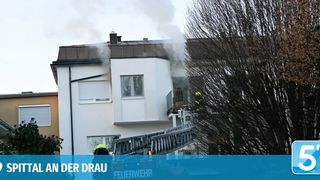 Feuerwehrleute reagieren auf einen Rauchvorfall in einem mehrstöckigen Wohngebäude. Rauch ist vom Schornstein und Dach sichtbar.