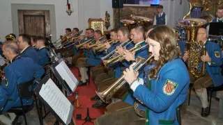 Eine Gruppe von Musikern spielt Trompeten in einer Kirche. Sie tragen alle blaue Uniformen. Die Frau vorne spielt eine Trompete und trägt ein Armband. Es gibt Notenständer mit Notenblättern.