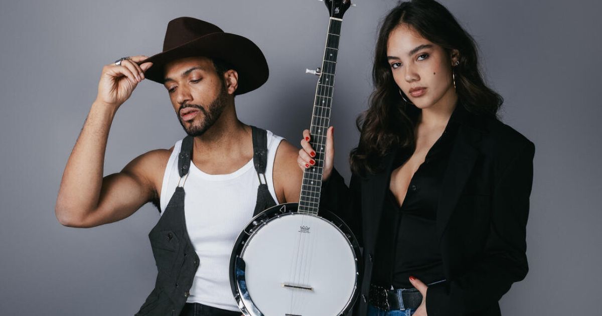 Ein Mann in einem Cowboyhut und eine Frau in einem schwarzen Mantel stehen eng beieinander und halten ein Banjo.