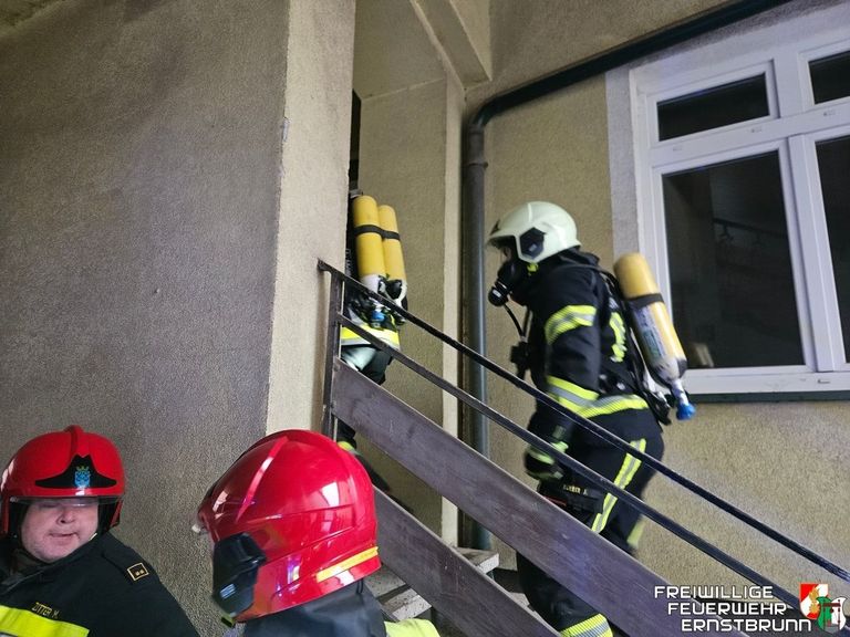 Feuerwehrleute in voller Ausrüstung, einschließlich Helme und Sauerstoffflaschen, steigen die Treppe hinauf. Einer ist unten, der andere oben.