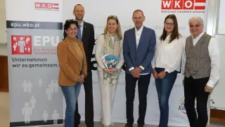 Fünf Personen posieren für ein Foto vor einem Banner. Das Banner zeigt das Logo der Wirtschaftskammer. Die Leute sind professionell gekleidet.