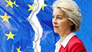 Eine Frau mit kurzen blonden Haaren steht vor einer zerrissenen Flagge der Europäischen Union und scheint ein Publikum anzusprechen.
