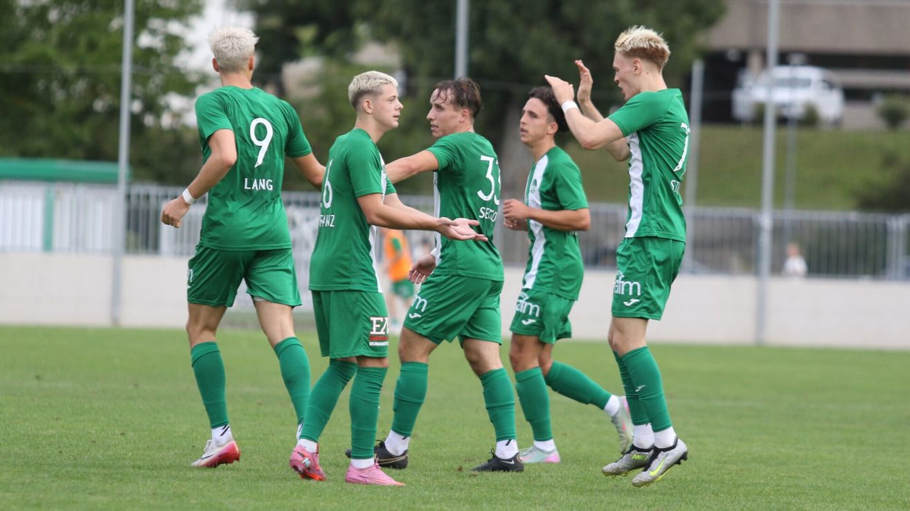 Fünf Fußballspieler in grünen Trikots feiern ein Tor auf dem Feld. Die Spieler haben Nummern auf ihren Trikots.