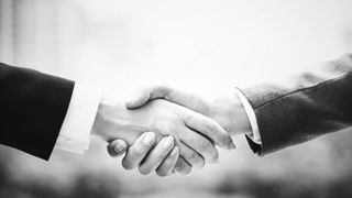 Zwei Personen in formeller Kleidung schütteln sich die Hände, möglicherweise um einen Geschäftsabschluss zu besiegeln.