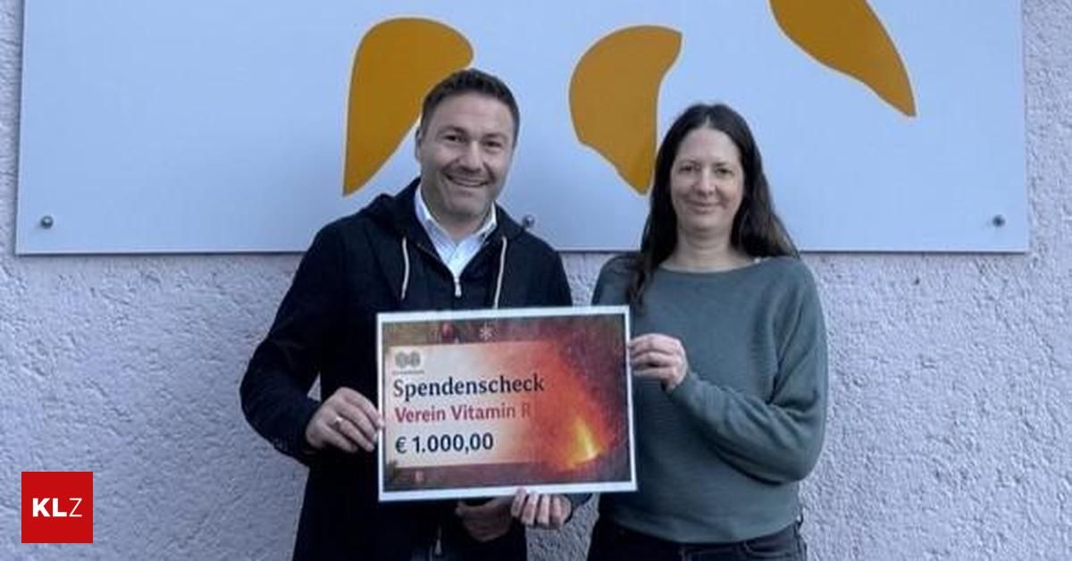 Ein Mann und eine Frau stehen nebeneinander und halten einen Spendenscheck. Sie lächeln beide und wirken glücklich. Der Mann trägt eine schwarze Jacke, und die Frau trägt einen grünen Pullover.