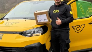 Ein Mann steht neben einem gelben Lieferwagen mit einer Box in den Händen. Er gibt einen Daumen hoch. Der Lieferwagen hat den Text OPS auf der Vorderseite und ein Logo an der Seite.