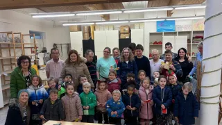 Eine Gruppe von Menschen, einschließlich Erwachsener und Kindern, steht in einem Raum. Sie alle lächeln und posieren für ein Foto. Im Hintergrund befinden sich Kisten und Regale.