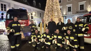 Eine Gruppe Feuerwehrleute posiert für ein Foto vor einem geschmückten Weihnachtsbaum und einem Feuerwehrauto.