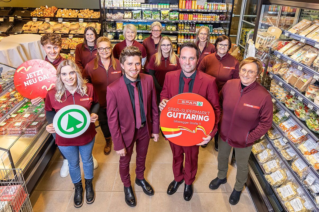 Eine Gruppe von Menschen in passenden roten Uniformen steht in einem Supermarkt. Sie posieren für ein Foto und halten ein Schild mit der Aufschrift 'SPAR-SUPERMARKT GUTTARING'.