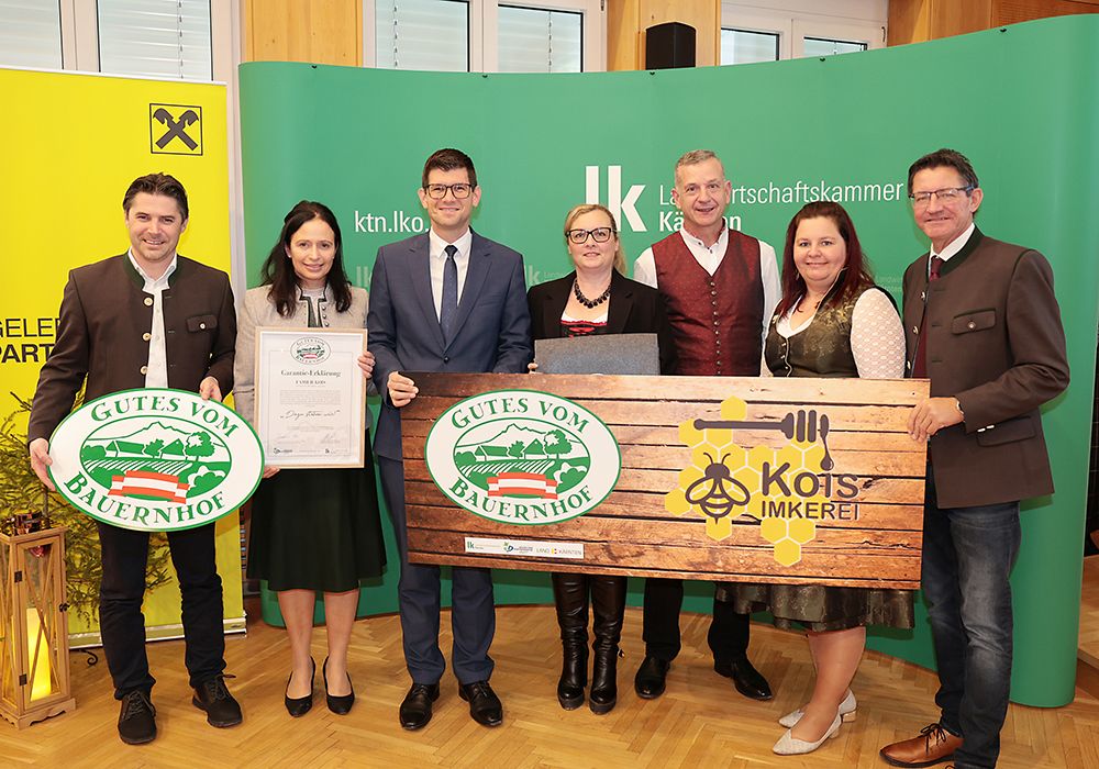 Eine Gruppe von Menschen, die ein Zertifikat und eine Plakette halten, posiert vor einem grünen Hintergrund. Sie tragen formelle Kleidung.