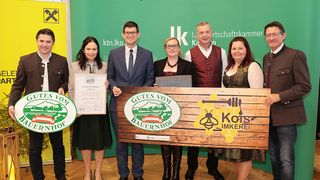 Eine Gruppe von Menschen, die ein Zertifikat und eine Plakette halten, posiert vor einem grünen Hintergrund. Sie tragen formelle Kleidung.