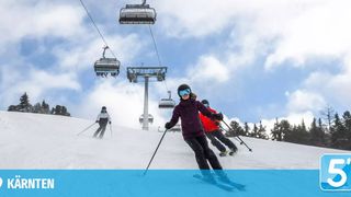 Skifahrer auf einem verschneiten Berg mit einer Skiliftanlage im Hintergrund. Bäume säumen den Hang.