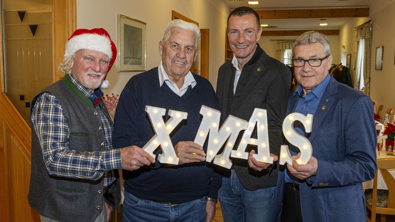 Vier Männer halten ein beleuchtetes XMAS-Schild hoch. Sie lächeln und scheinen für ein Foto zu posieren.