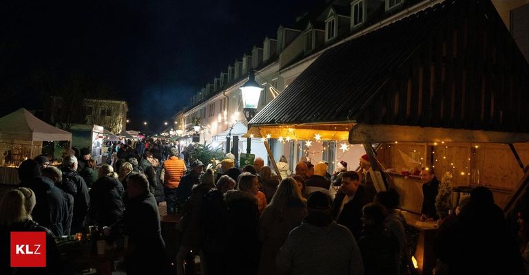 Bei Nacht ist eine belebte Straße von Menschen gesäumt, einige tragen Mützen, stehen um Stände mit Lichtern und Dekorationen. Ein Mann in einem Weihnachtsmannhut steht bei einer Bar.