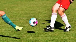 Ein Fußballspieler in roten Shorts und weißen Socken tritt einen Ball mit einem farbenfrohen Design.