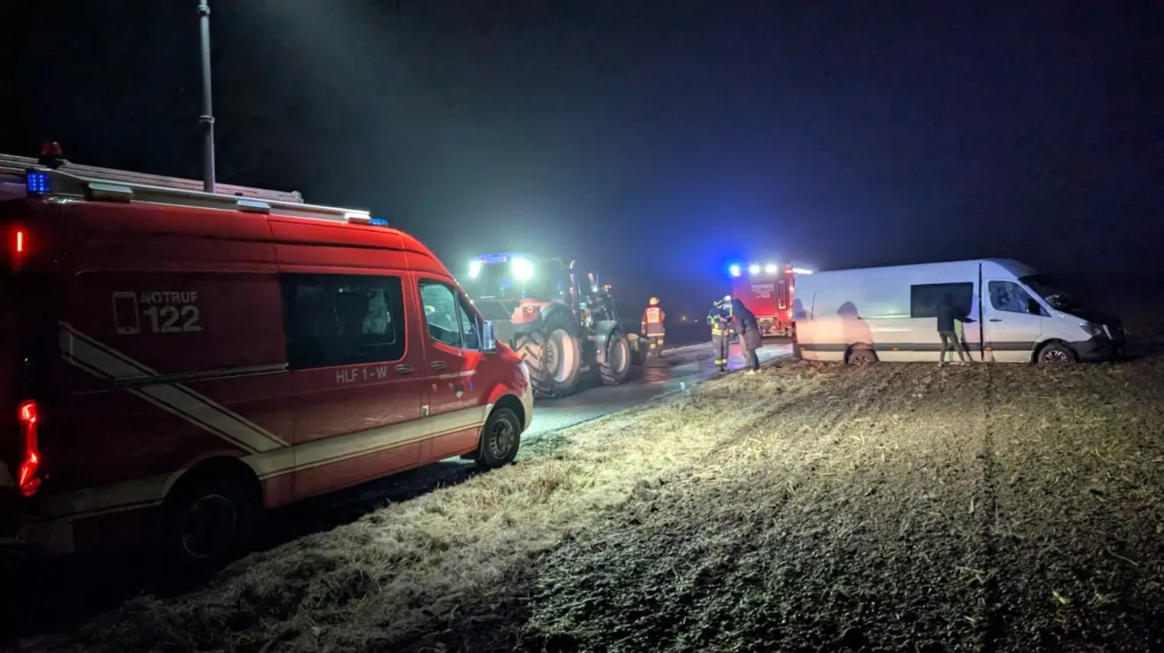 Ein rotes Notfallfahrzeug ist am Straßenrand geparkt. Ein weißer Van steht am Straßenrand mit einem Traktor und einigen Leuten, die in der Nähe stehen. Der Himmel ist dunkel.