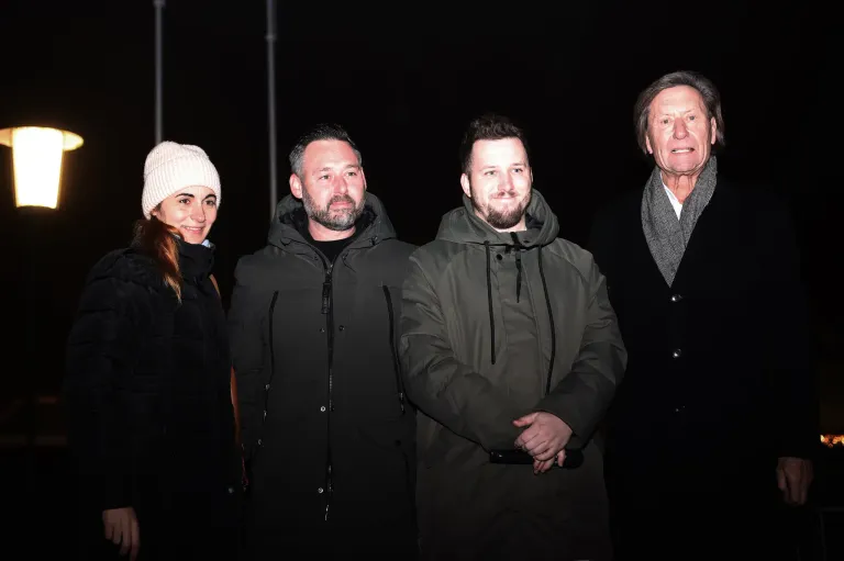 Vier Personen posieren nachts für ein Foto, alle tragen Jacken. Die Frau trägt eine weiße Mütze und die Männer Schals.