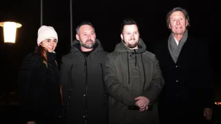 Vier Personen posieren nachts für ein Foto, alle tragen Jacken. Die Frau trägt eine weiße Mütze und die Männer Schals.